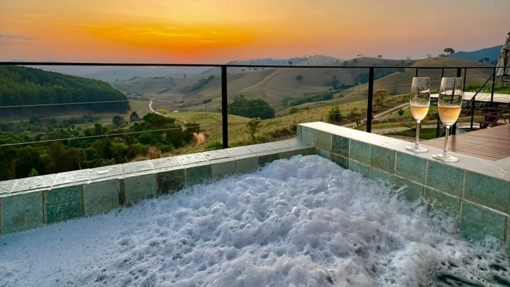 A piscina de borda infinita de azulejo esmeralda na hora dourada, com o sol baixo sobre os morros