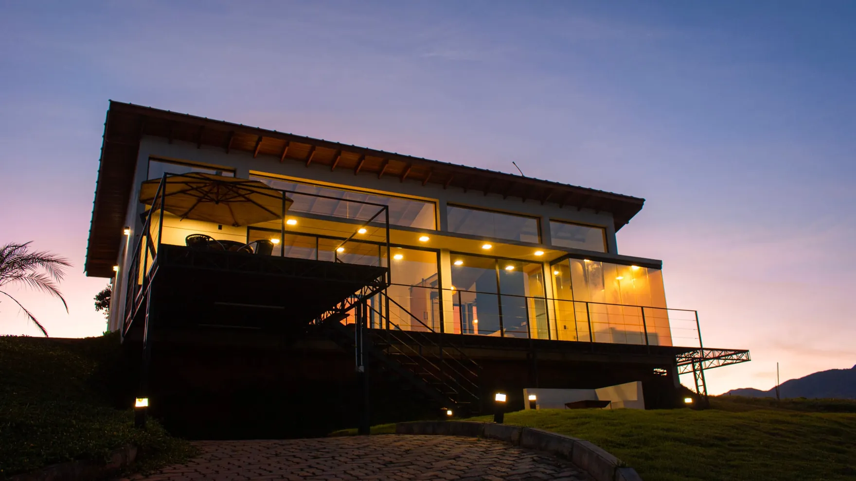 A casa de vidro do Solarium acesa ao anoitecer, brilhando na crista da serra