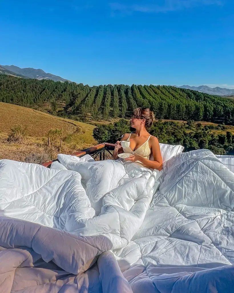 Cama de roupa branca de frente para o vale pela parede de vidro