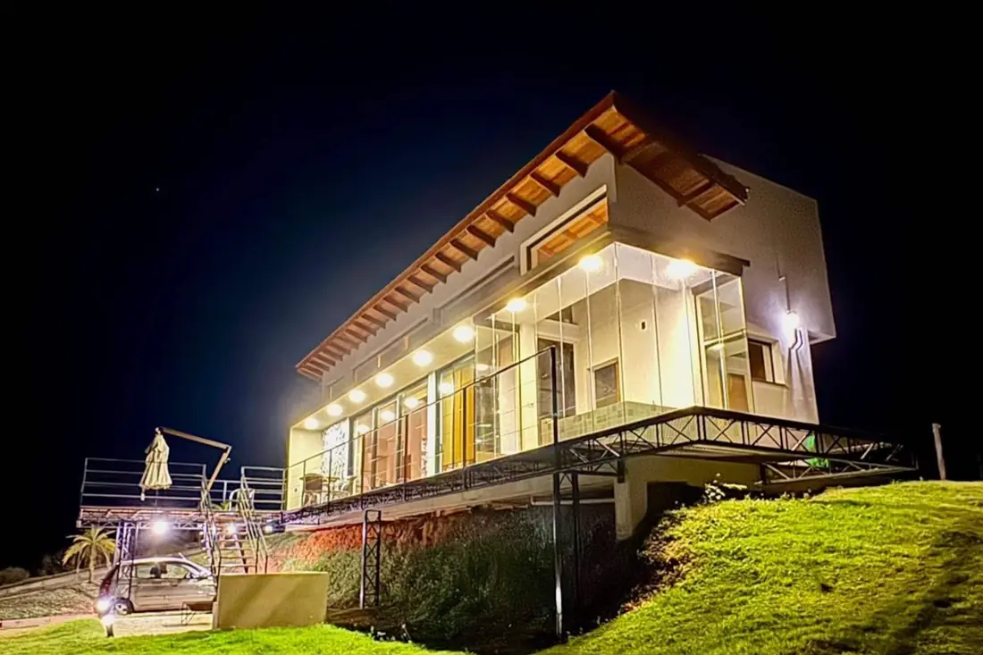 Casa de vidro acesa na crista da serra ao anoitecer